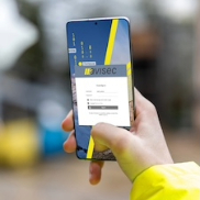 Person holding a smartphone with the login screen for the avisec Cloud Cockpit open, accessing camera data in an outdoor setting.